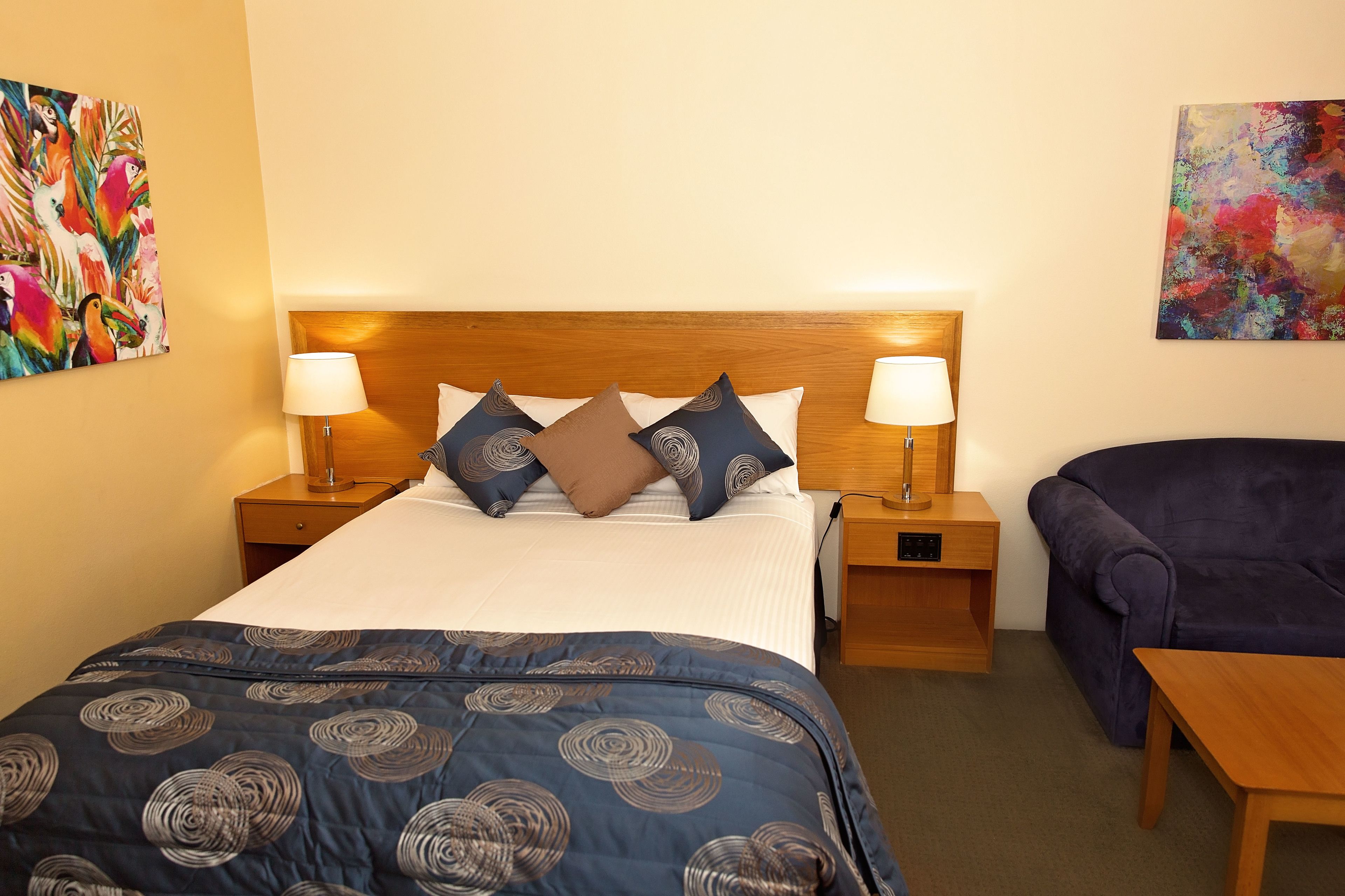 A hotel room with a bed, two bedside tables with lamps, a purple sofa, and a wooden nightstand.