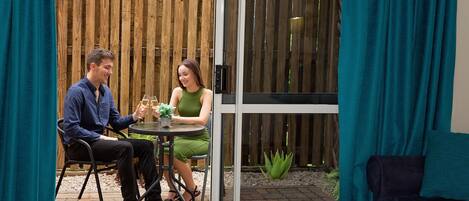 Una pareja sentada en una mesa al aire libre, con vista a una valla de madera y un ventanal.