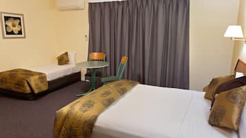 Ein Hotelzimmer mit zwei Einzelbetten, einem kleinen runden Tisch, einem Stuhl und einem großen Fenster mit Vorhängen.