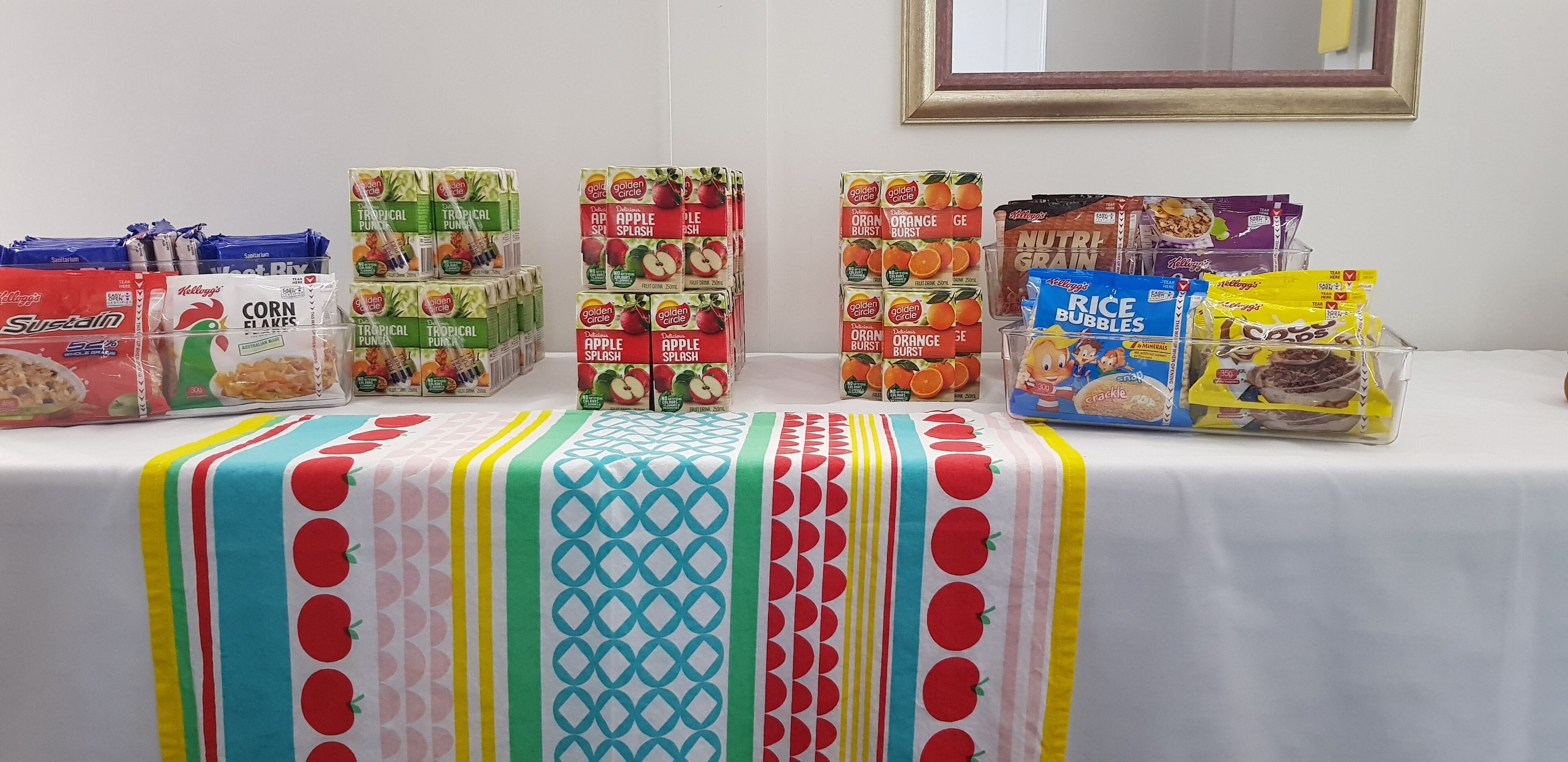 Een tafel met diverse etenswaren, waaronder ontbijtgranen, vruchtensappen en rijstvlokken.