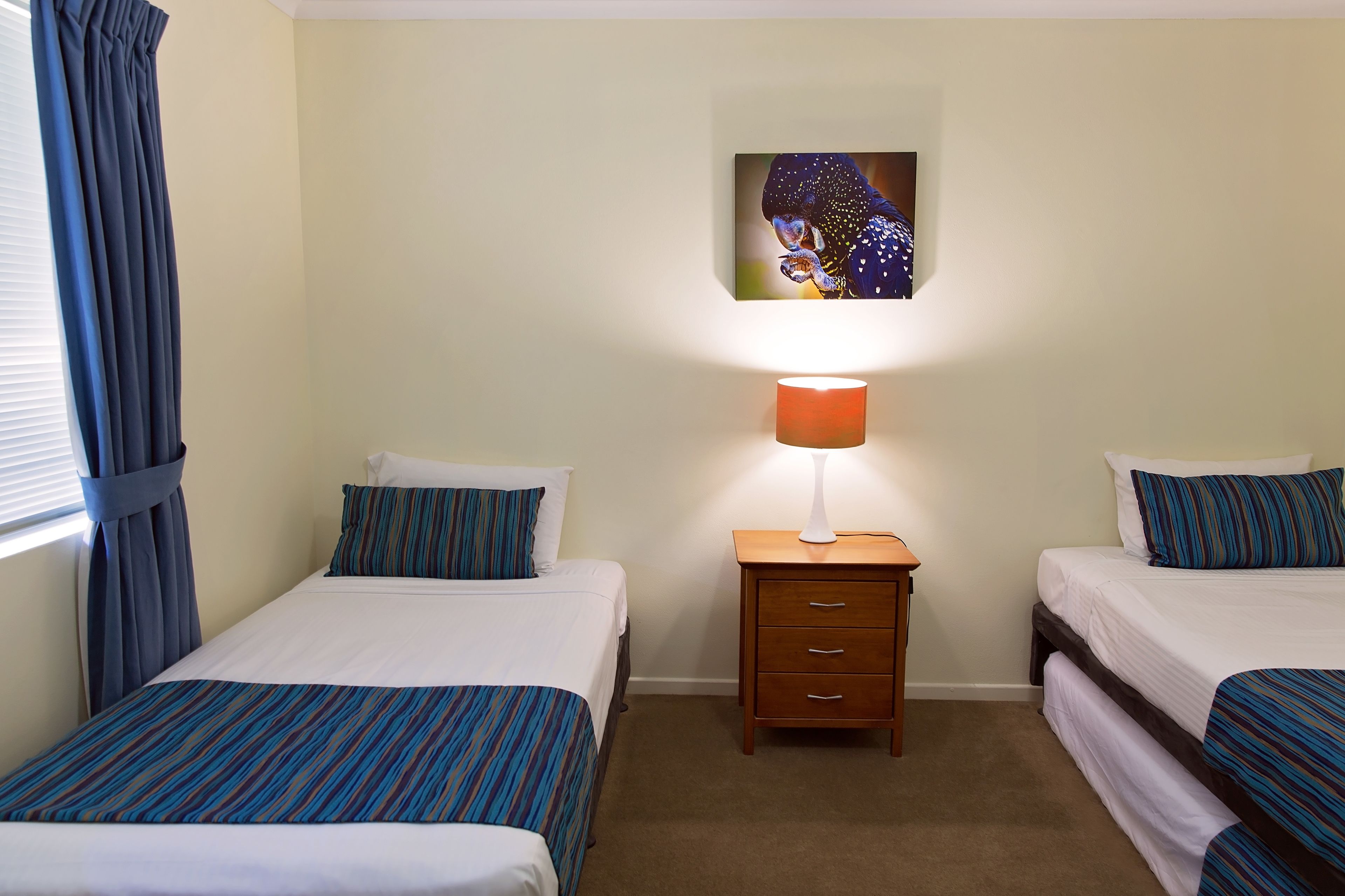 A hotel room with two beds, a nightstand with a lamp, and a painting on the wall.