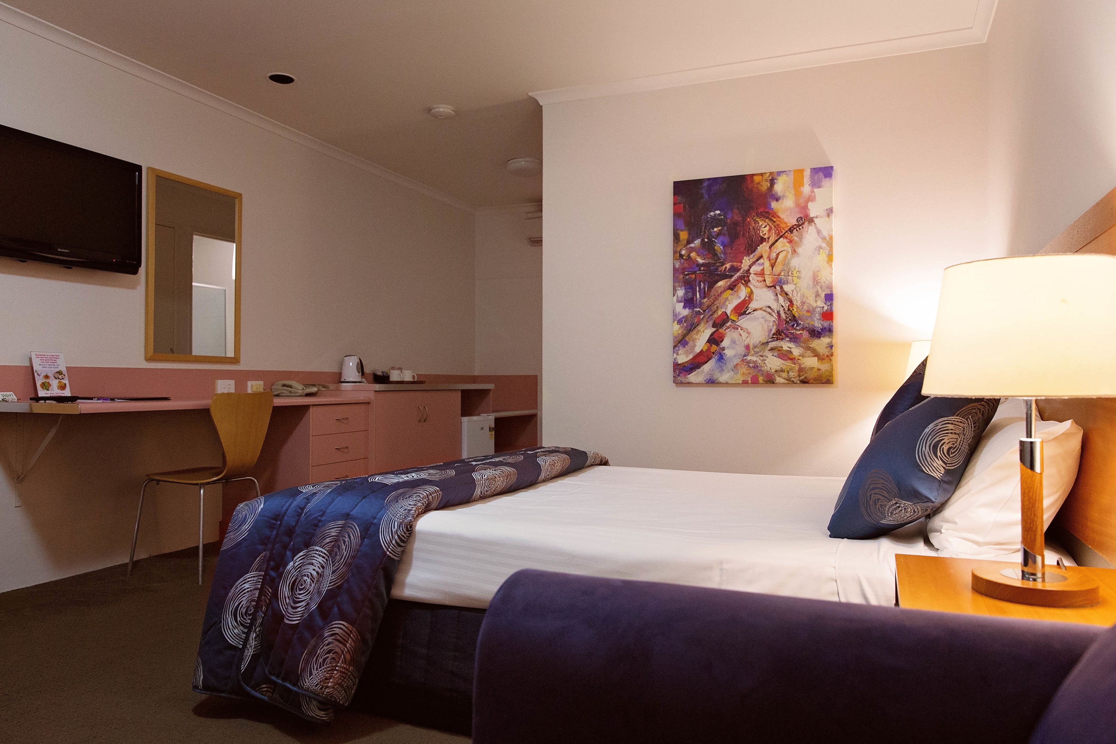 Una camera d'albergo con un letto, una scrivania, una sedia, una televisione e un quadro appeso al muro.