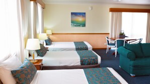 A hotel room with two beds, a green sofa, a dining table, and a painting of a sunset. - White Lace Motor Inn (West Mackay)