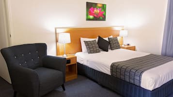 Une chambre d’hôtel comprenant un lit, deux tables de chevet avec des lampes, une chaise et un tableau représentant une fleur accroché au mur.