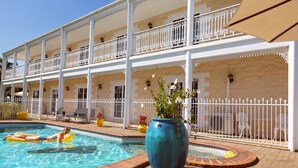 A pool area with a person on a float, a large vase with flowers, and a white fence. - White Lace Motor Inn (West Mackay)