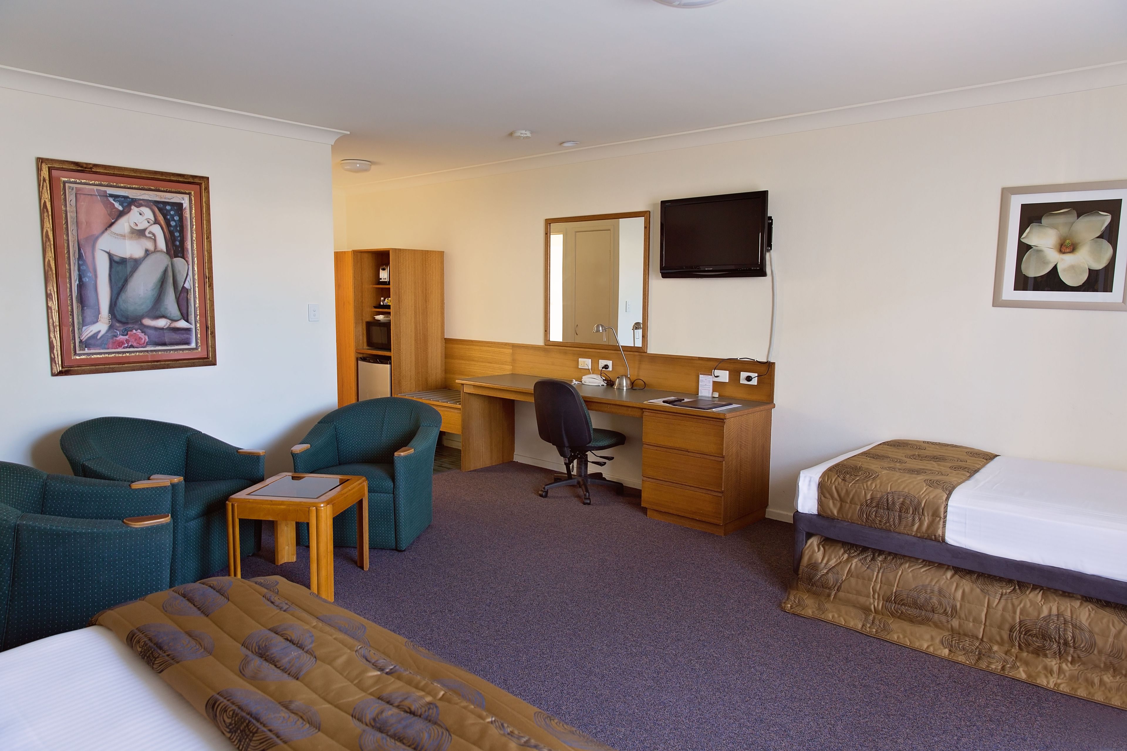 Ein Hotelzimmer mit einem Bett, zwei Stühlen, einem Schreibtisch, einem Computer, einem Fernseher und einem Bücherregal.