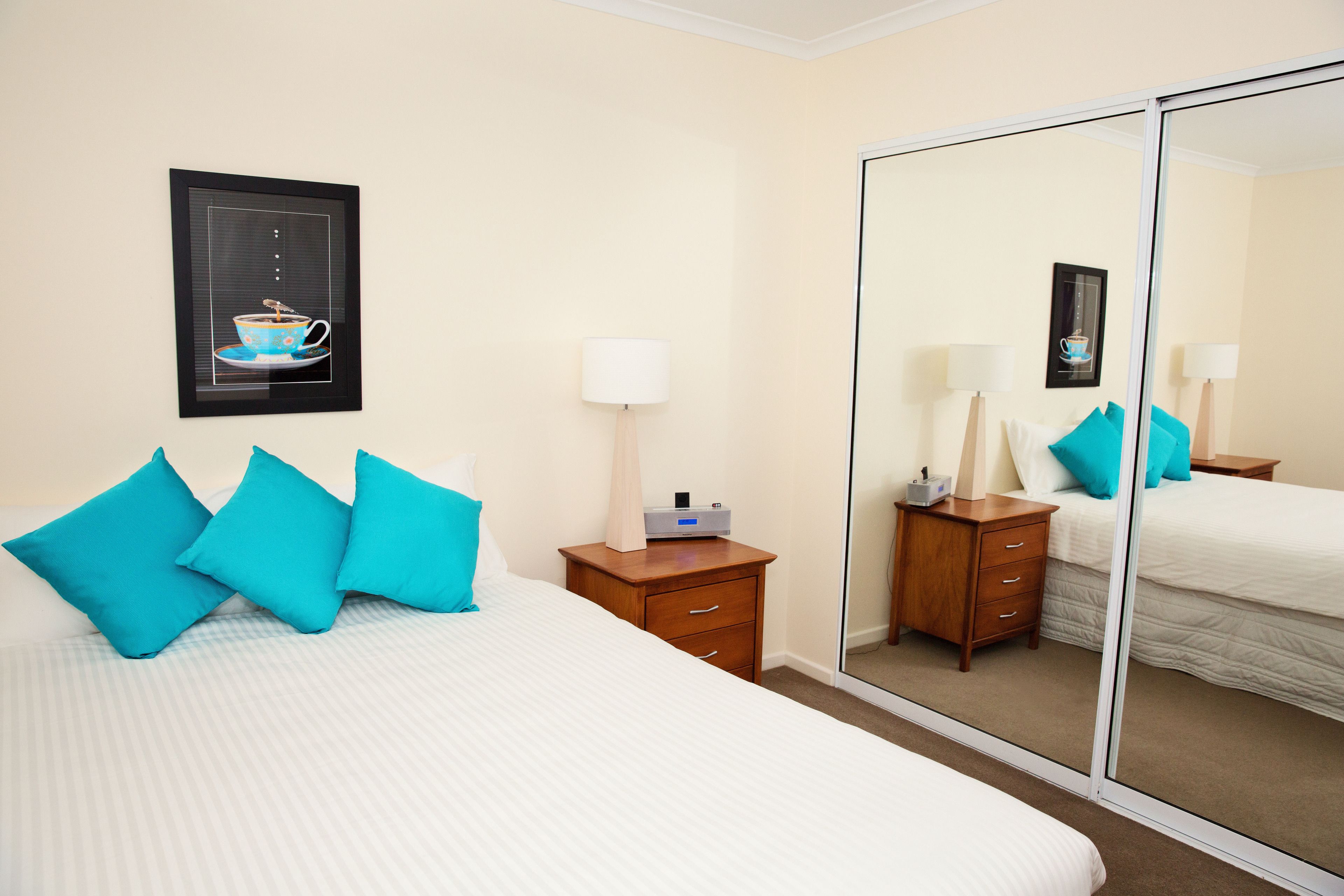 A hotel room with a bed, a nightstand, a mirror, and a framed picture on the wall.