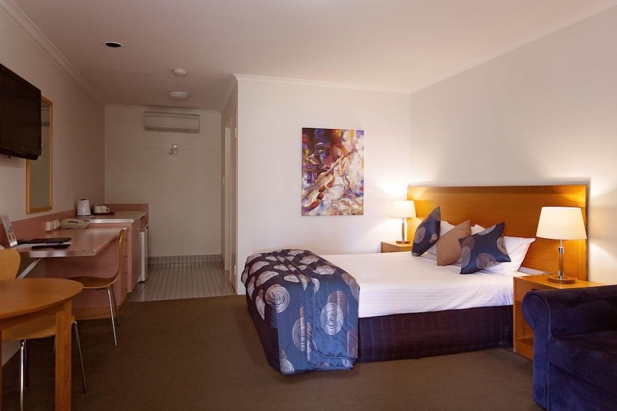 A hotel room with a bed, bedside tables, a desk, and a chair.