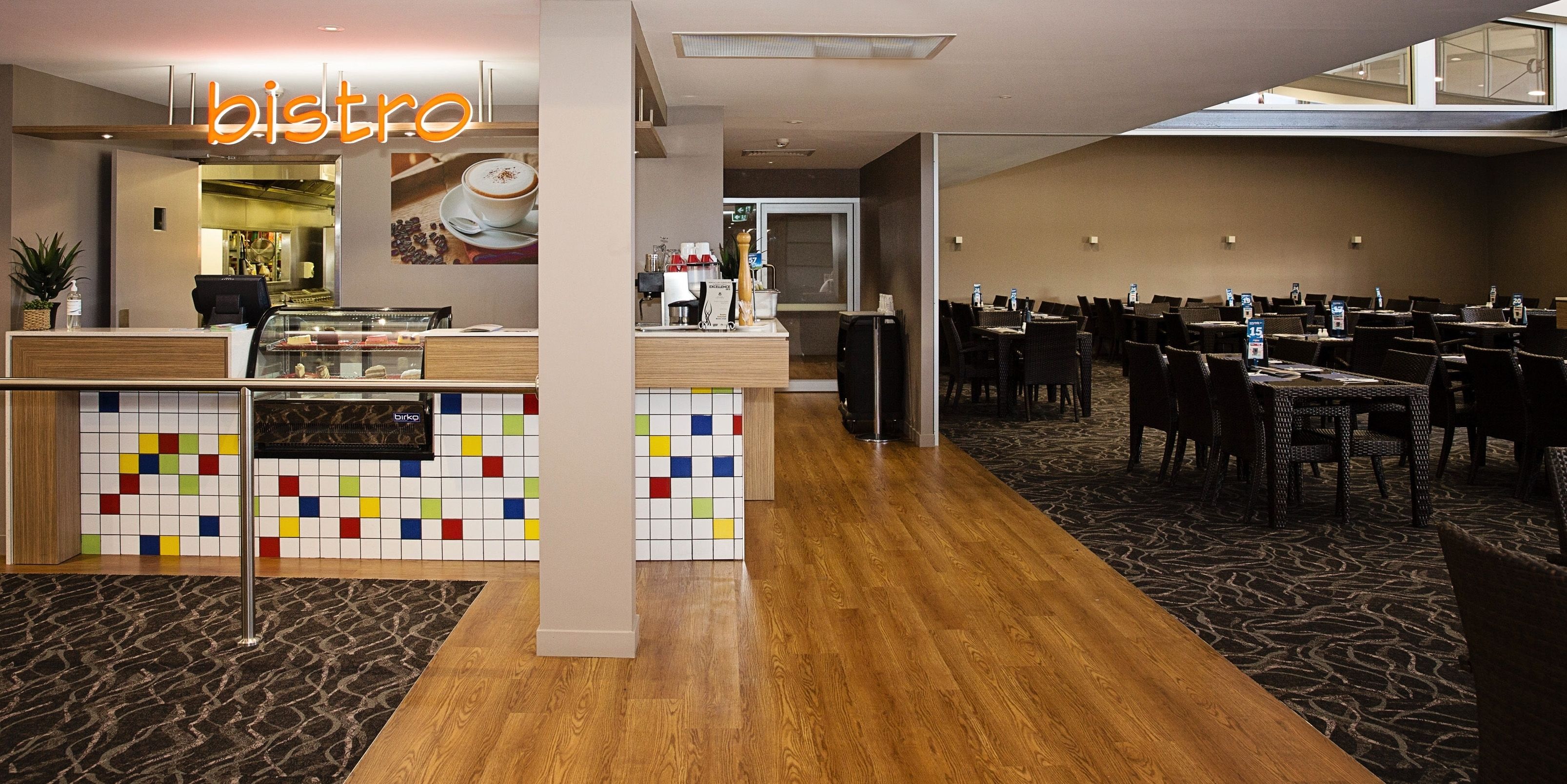 A bistro with a colorful tile wall, a reception desk, and a dining area with tables and chairs.