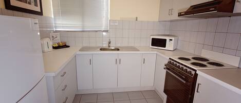 A compact kitchen with white cabinets, a built-in microwave, a stove, and a sink.