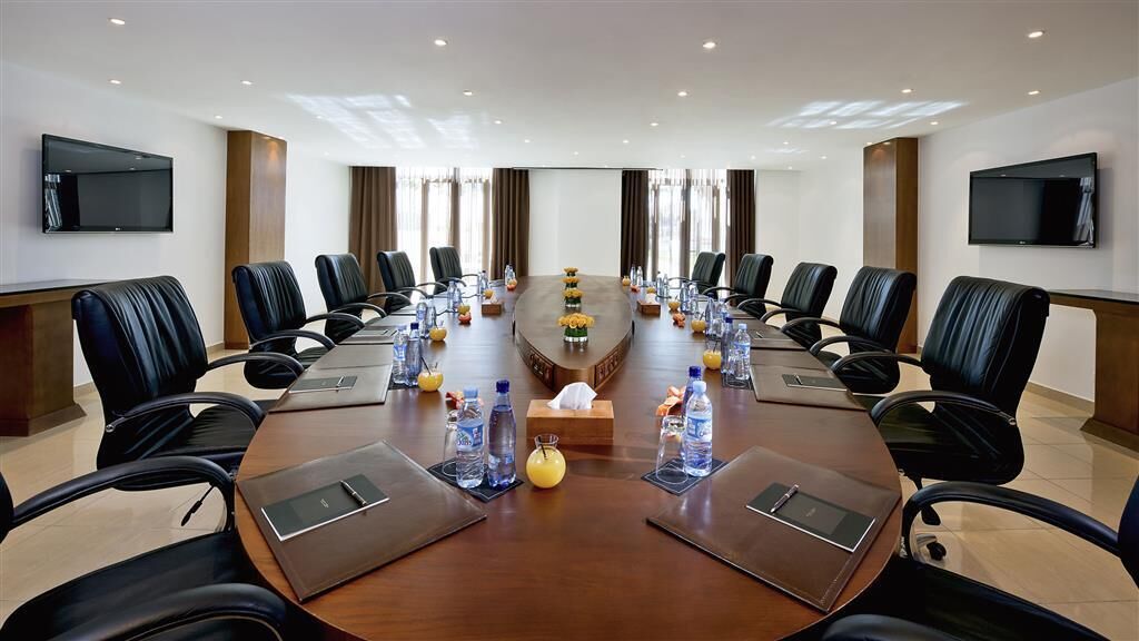 A conference room with a long table, black leather chairs, water bottles, and a flower vase.