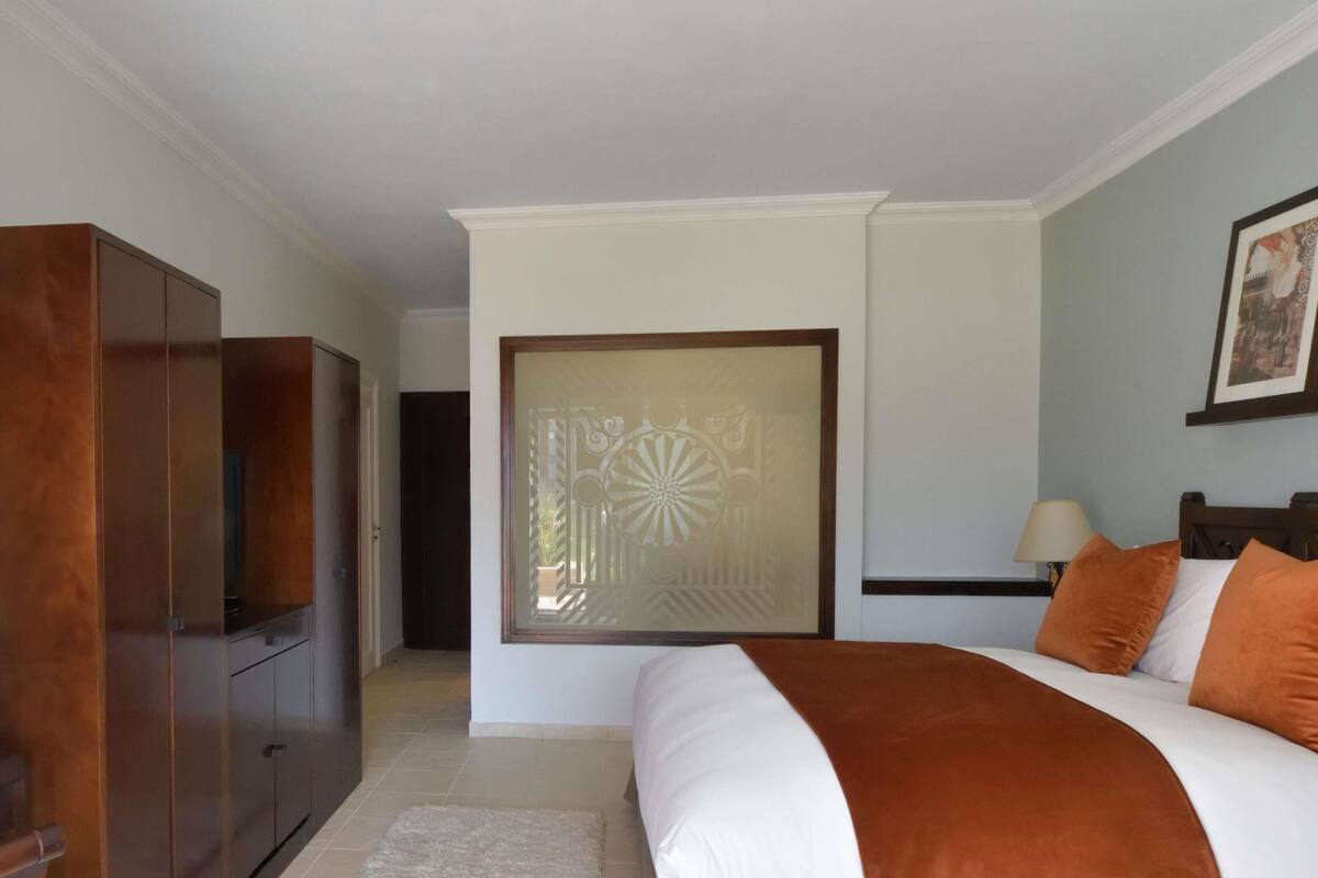 A bedroom with a bed, a wardrobe, a door with a decorative panel, and a painting on the wall.