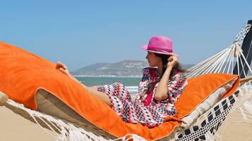 A hammock with an orange cushion on a beach with a clear sky and distant mountains.