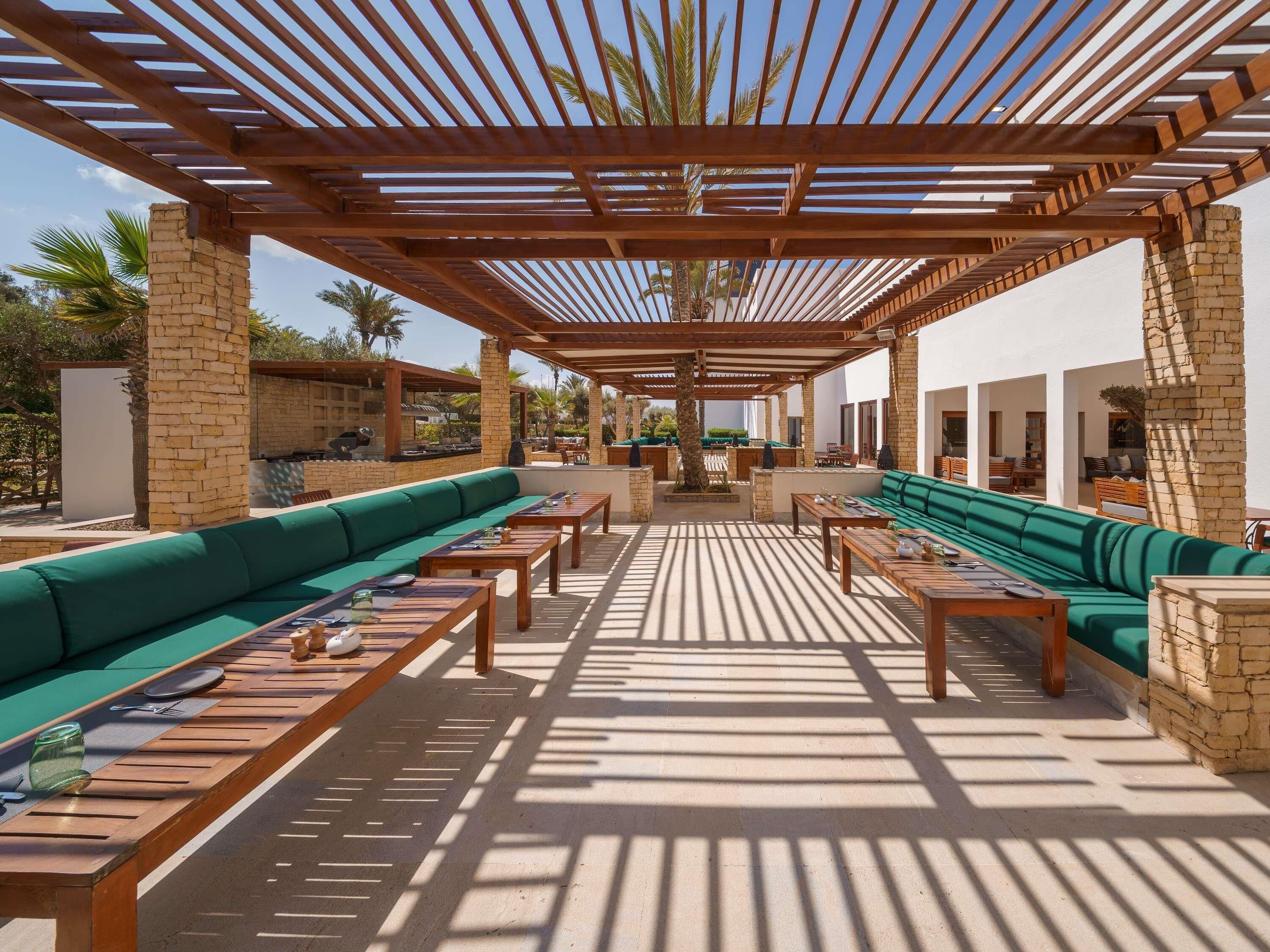 An outdoor patio with wooden pergolas, green sofas, and tables.