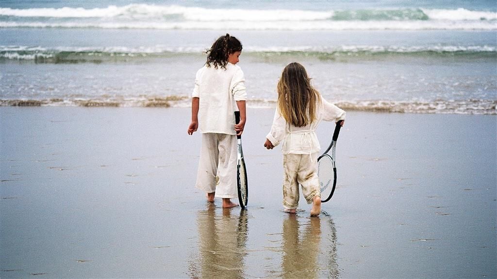 Dos niños caminando por una playa con una bicicleta.