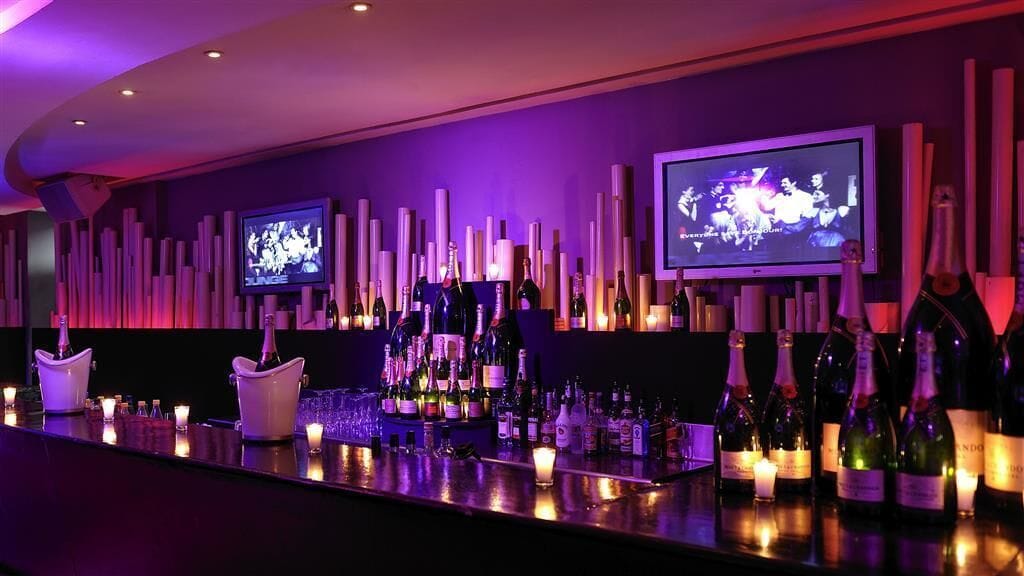 A bar area with multiple televisions, bottles of wine, and candles.