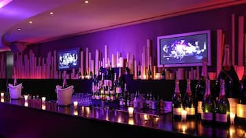 A bar area with multiple televisions, bottles of wine, and candles.