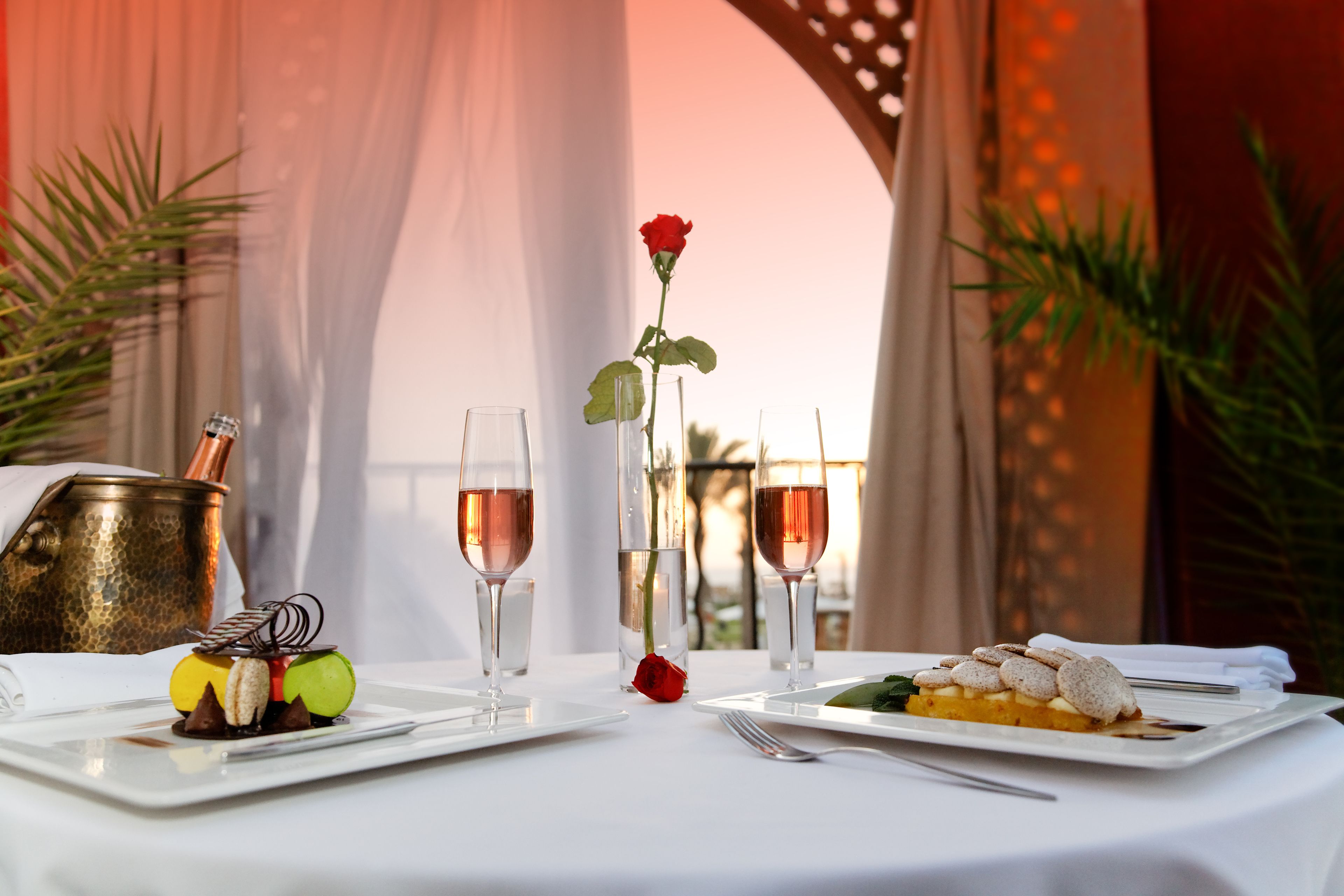 A table set for a meal with a dessert, a rose, and glasses of wine.