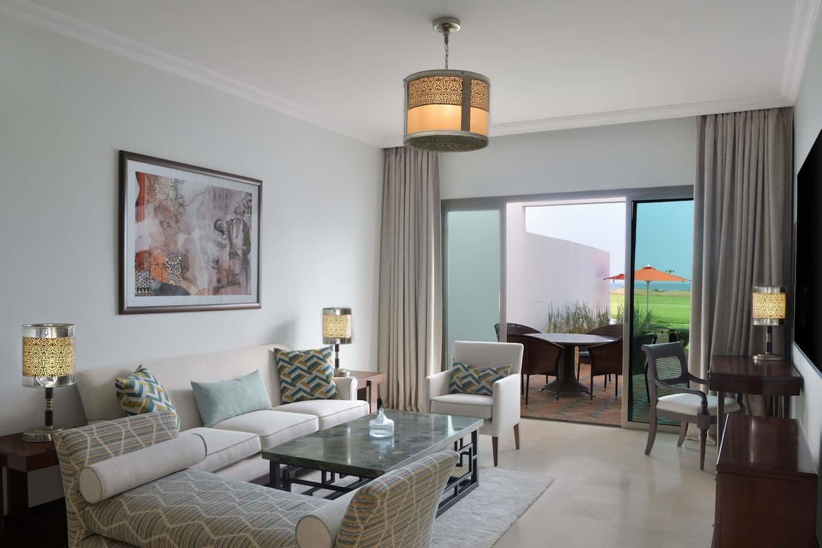 A modern living room with a sofa, coffee table, and lamps, a dining area with chairs, and a large window with a view.