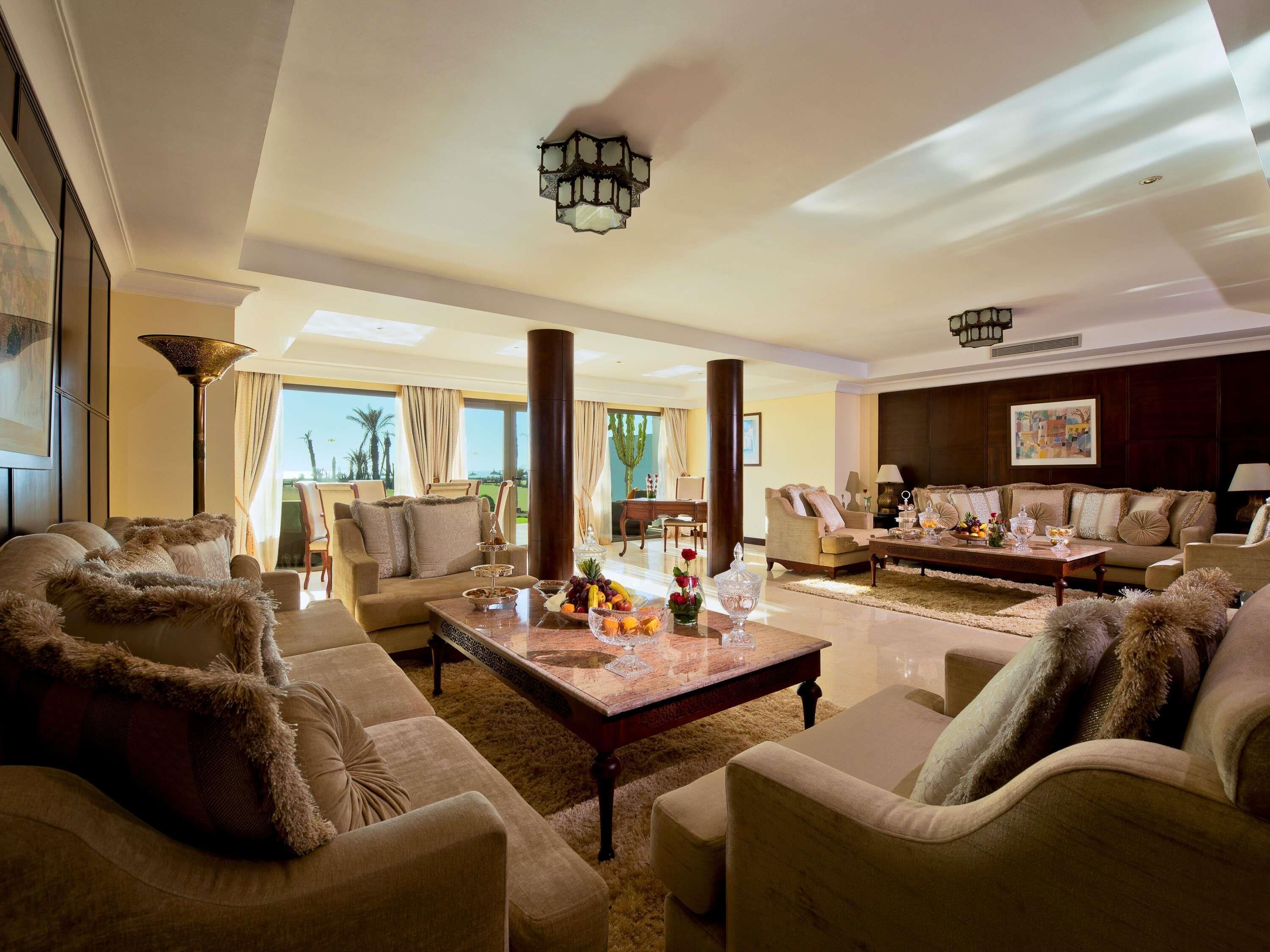 A spacious living room with multiple seating areas, a coffee table with fruit, and a view of the outdoors.