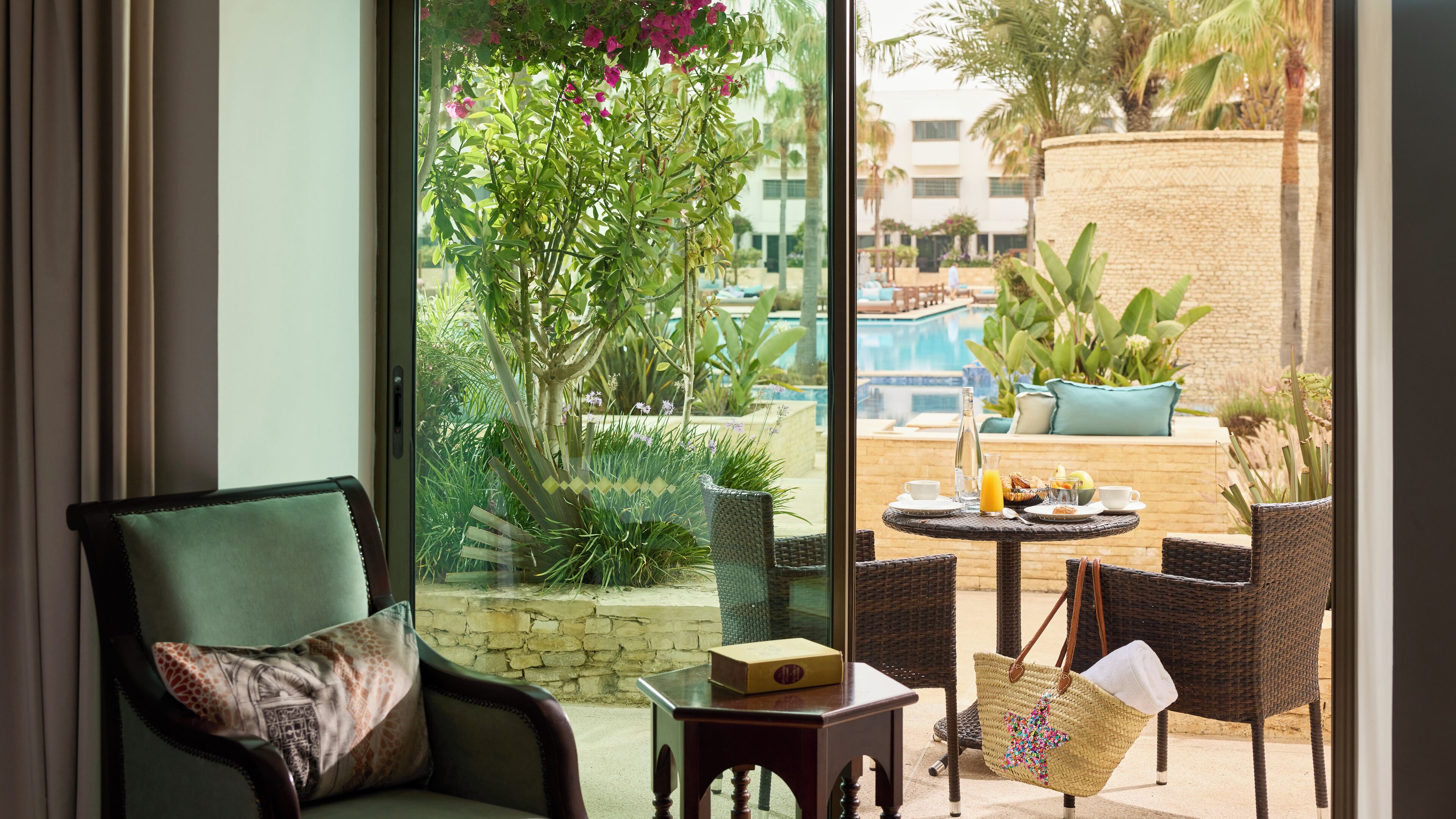 A room with a view of a pool, outdoor seating, and greenery.