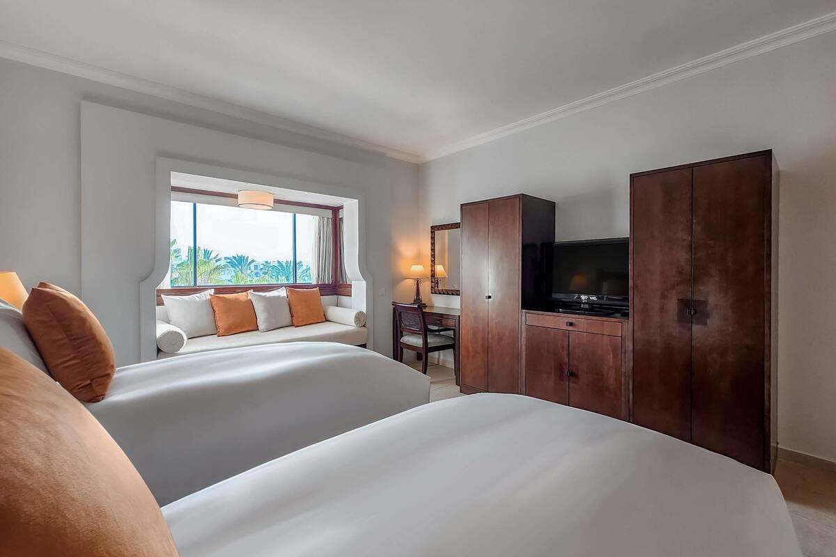 A hotel room with two beds, a TV, a desk with a chair, and a wardrobe.