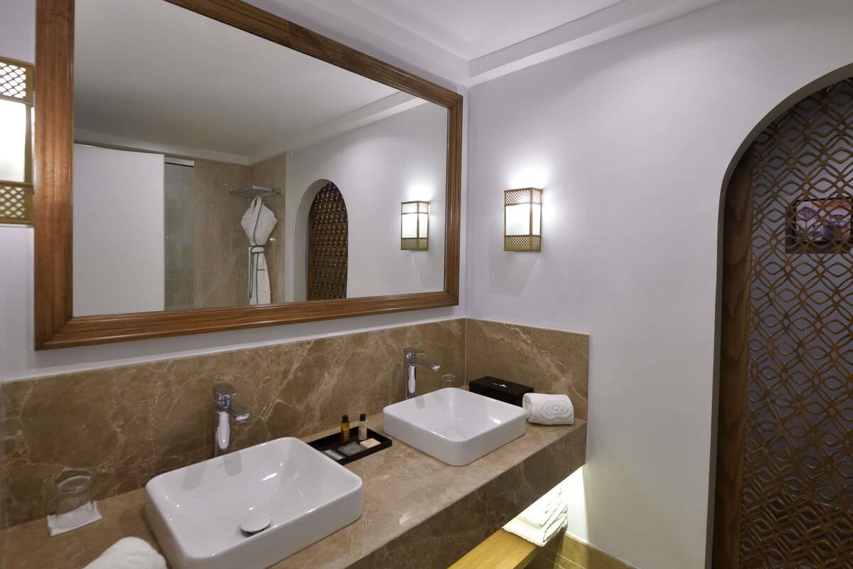 A bathroom with two sinks, a large mirror, and wall-mounted lights.