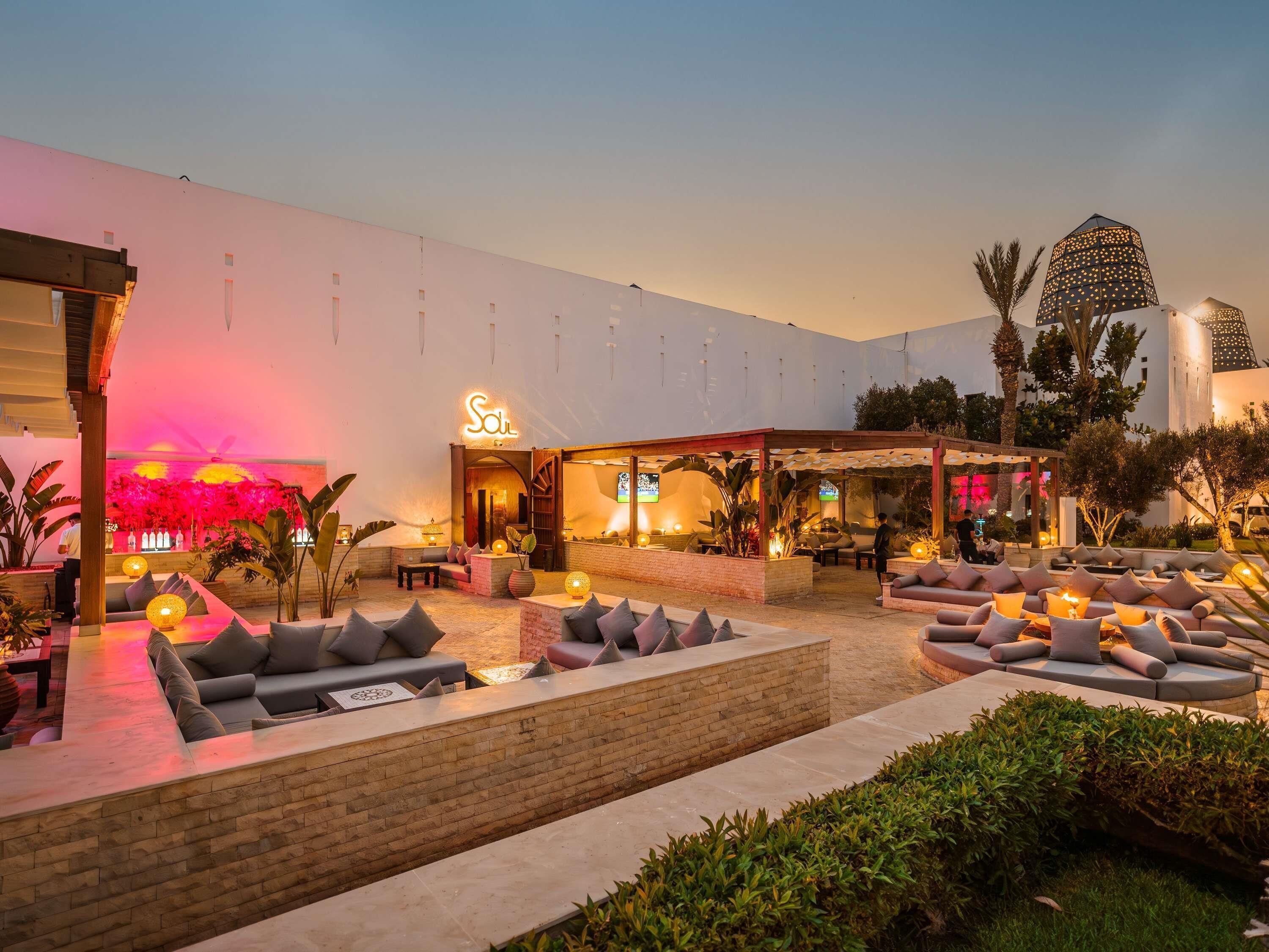 A hotel courtyard with outdoor seating, a covered area, and a prominent building with a sign.