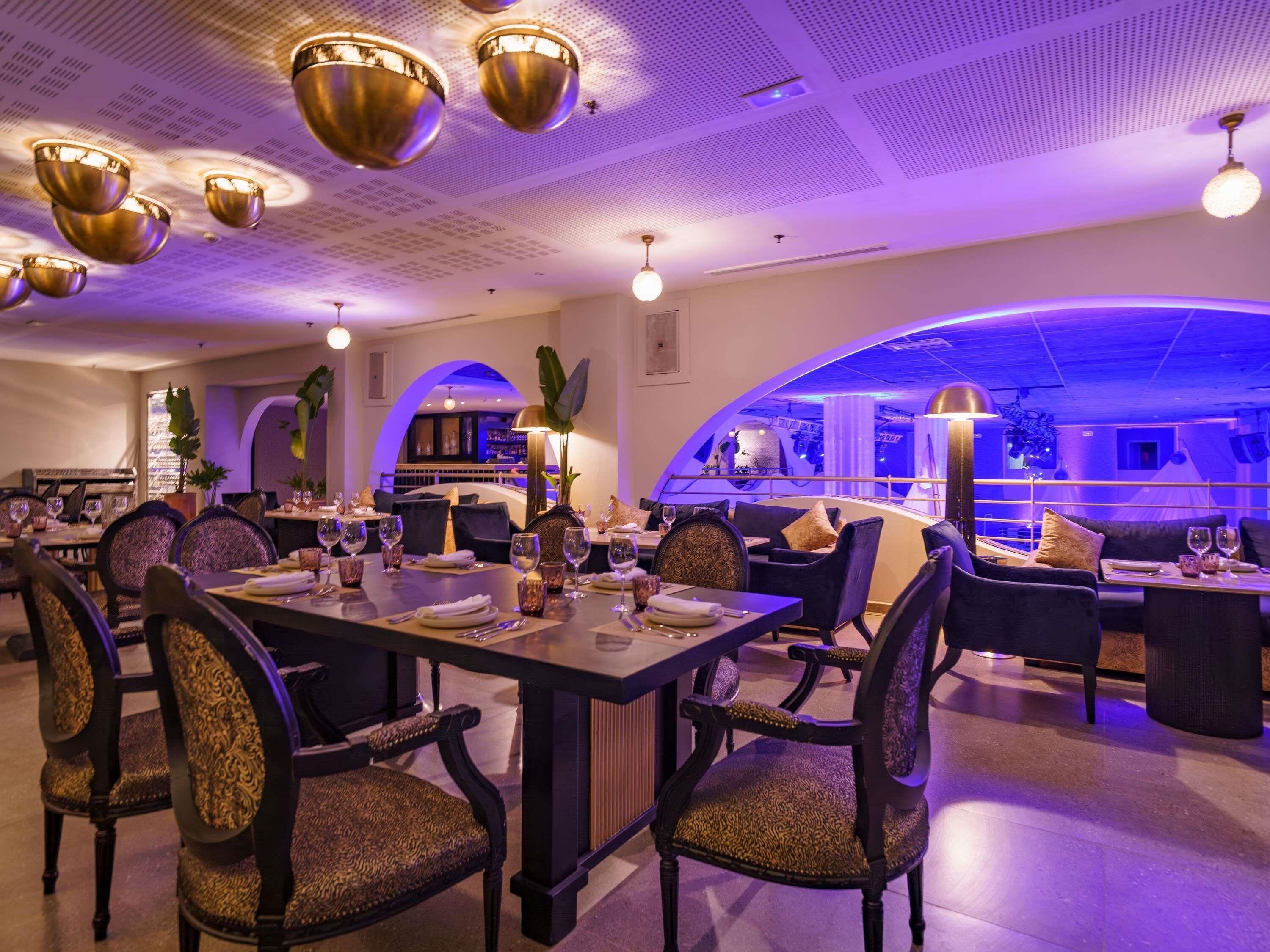 Un restaurante con una decoración moderna, que incluye mesas y sillas, una zona de bar y un diseño de techo original.