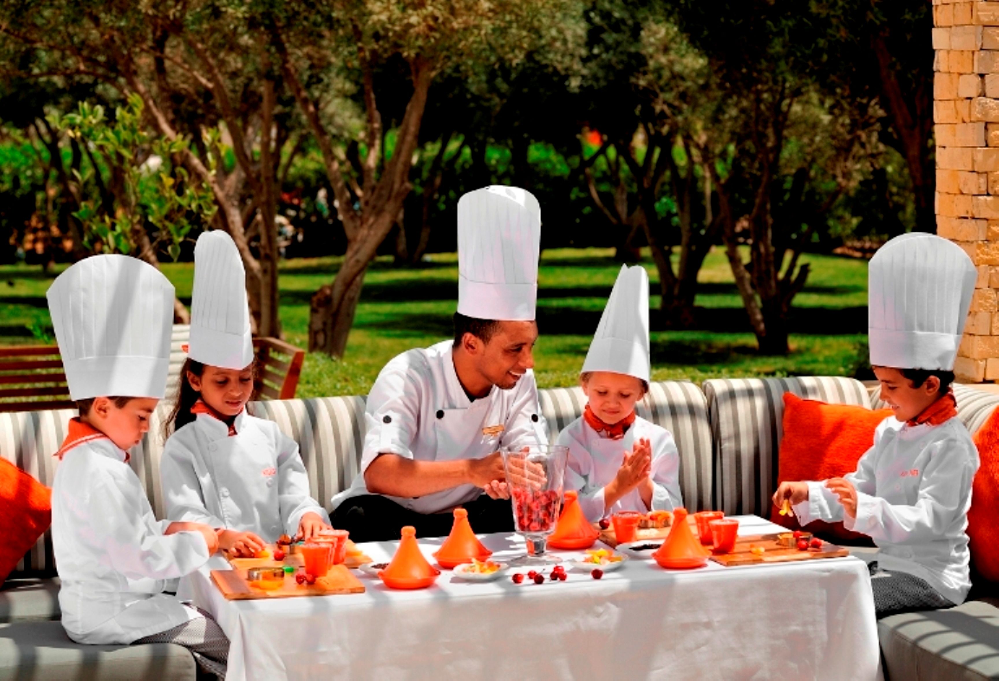 A group of people in chef uniforms seated at an outdoor table with food and drink items.