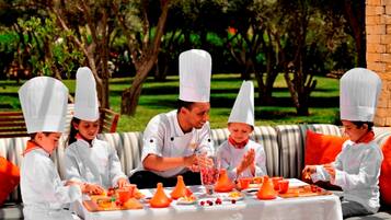 A group of people in chef uniforms seated at an outdoor table with food and drink items.