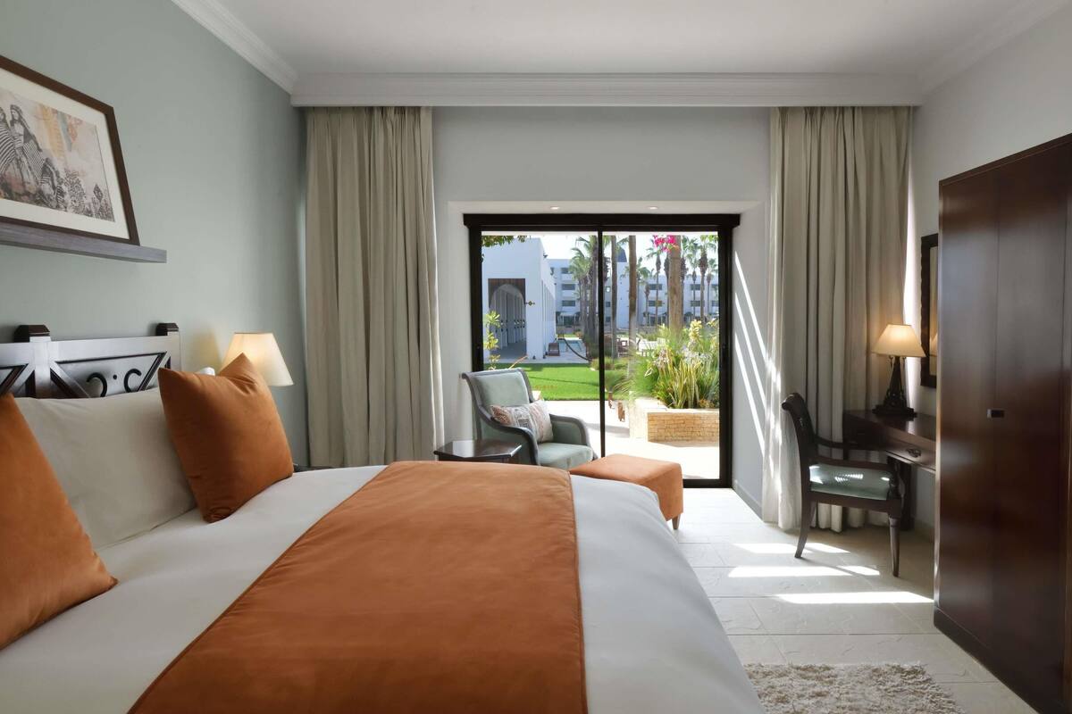 A hotel room with a large bed, a desk, a chair, and a view of the outdoors.