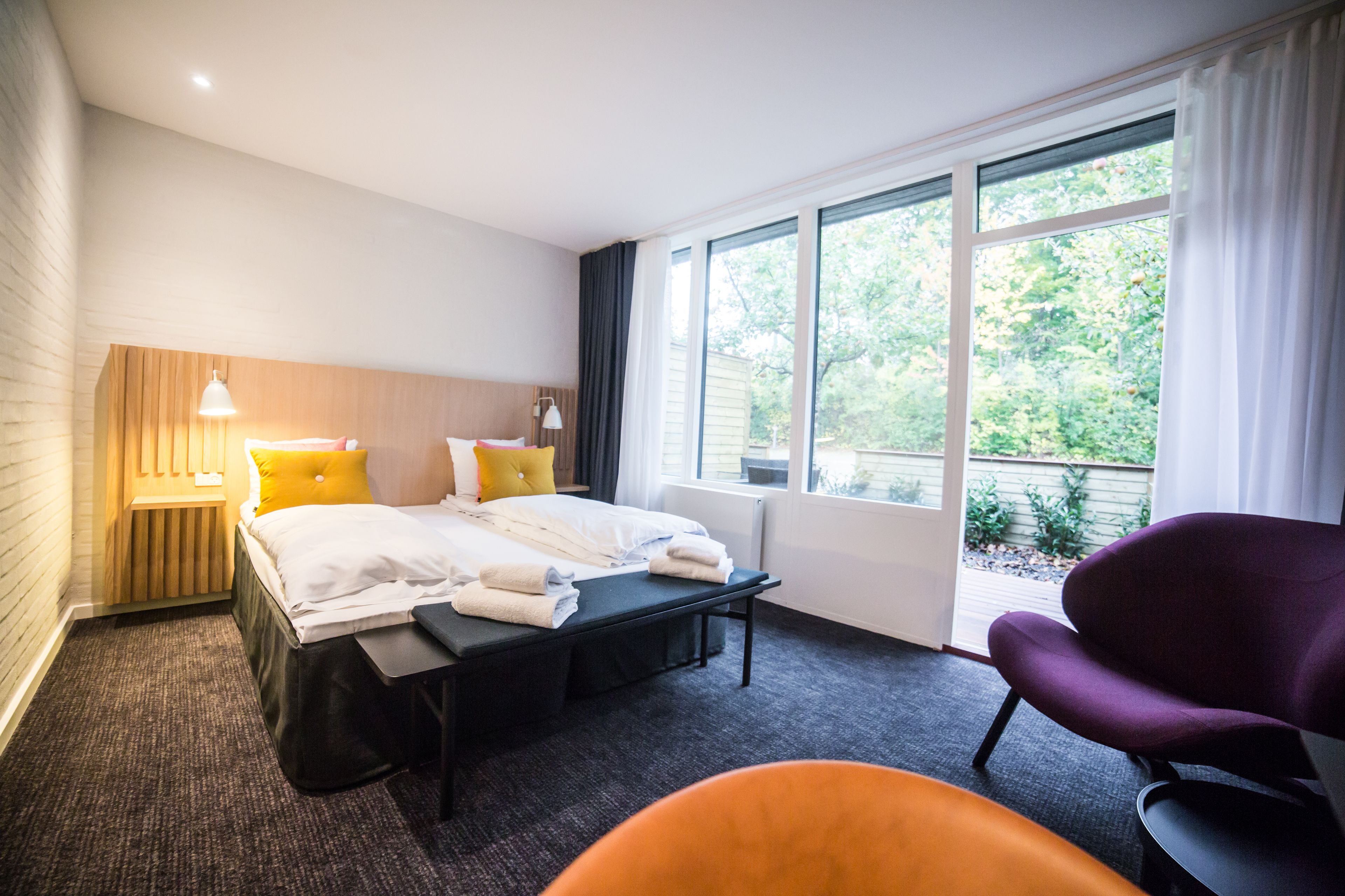 A hotel room with a bed, a desk, a chair, and large windows.