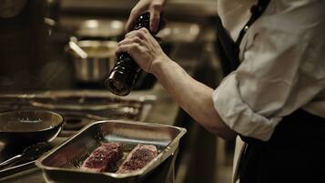 A chef seasoning steaks on a grill pan in a kitchen.