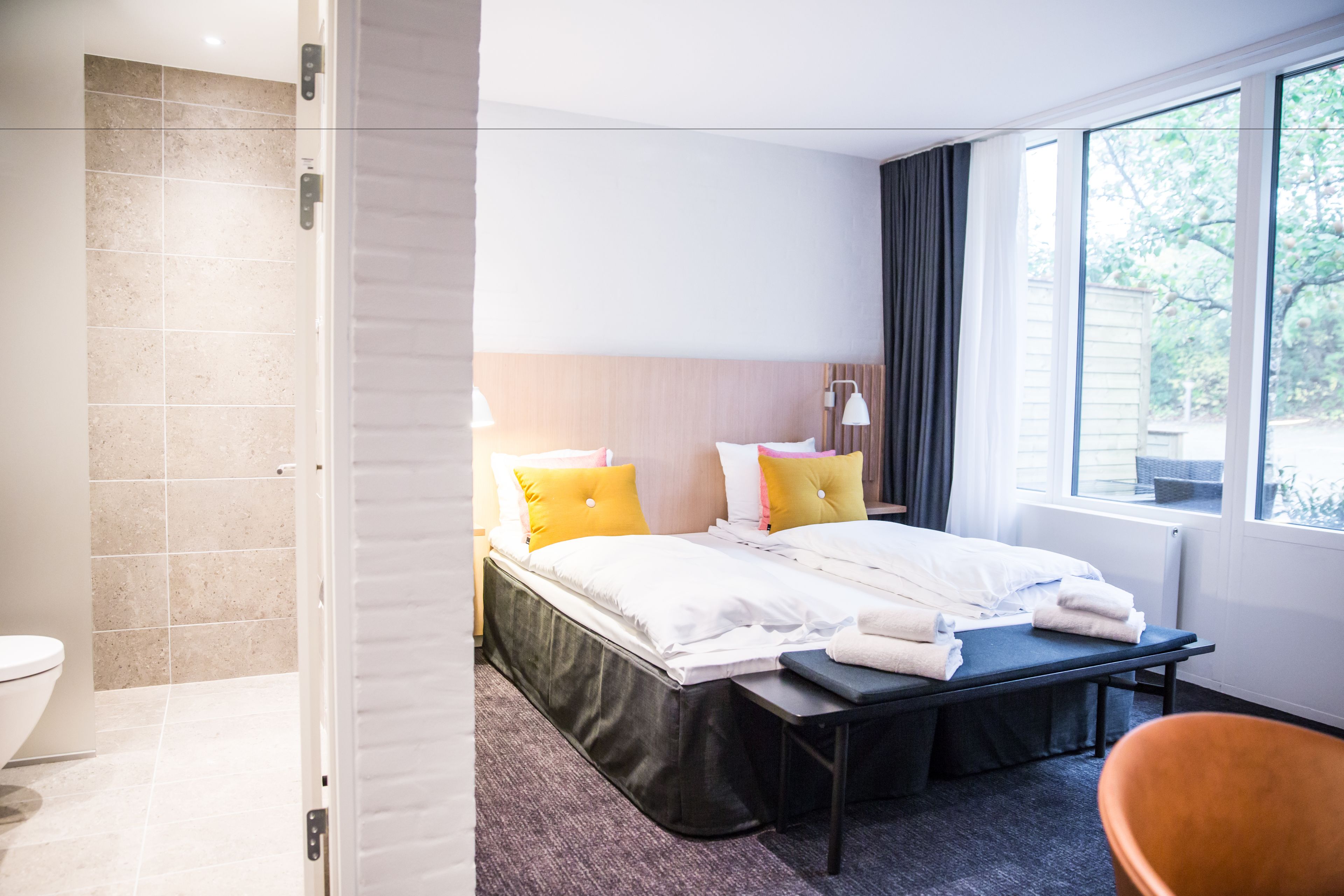 Quarto de hotel com cama, mesa de cabeceira e vista para o exterior.