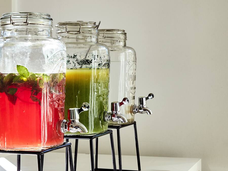 Trois bocaux en verre contenant des liquides de couleurs différentes, chacun muni d’un robinet en métal.