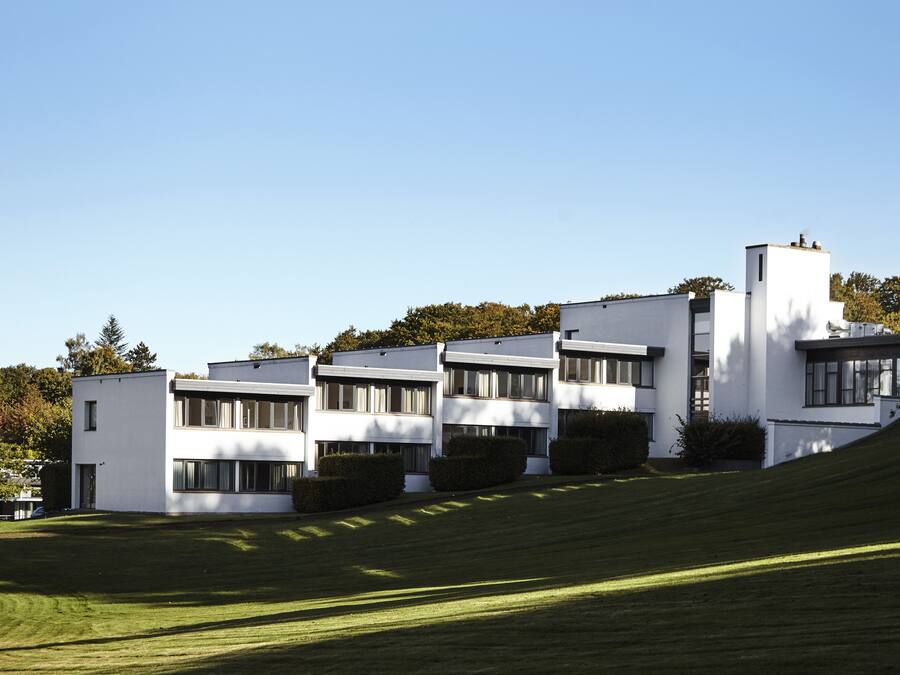 Un edificio moderno con techo plano, ventanas grandes y un césped cuidado.