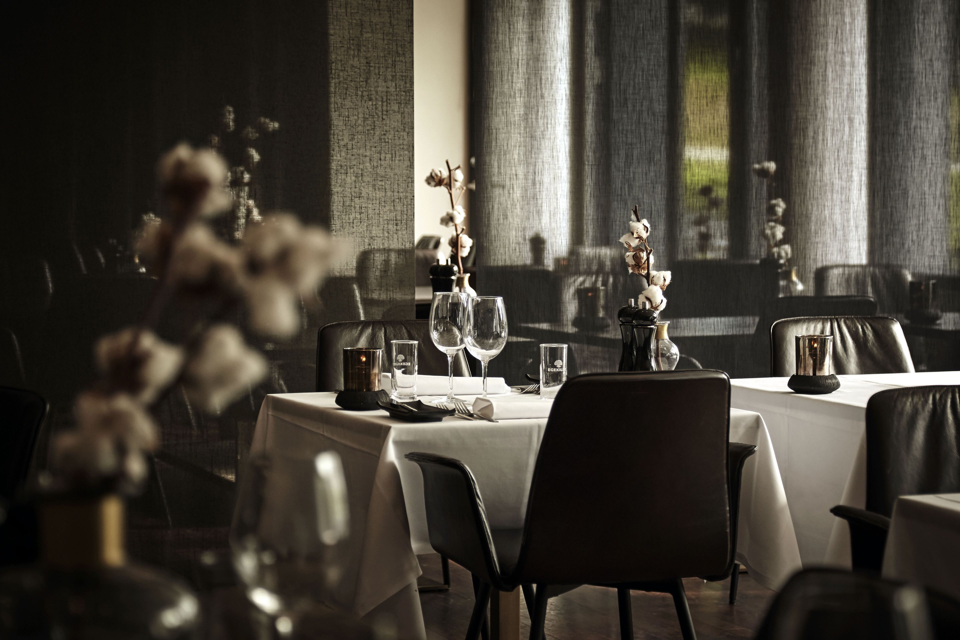 En restaurant med dækkede borde, en blomstervase og vinglas.