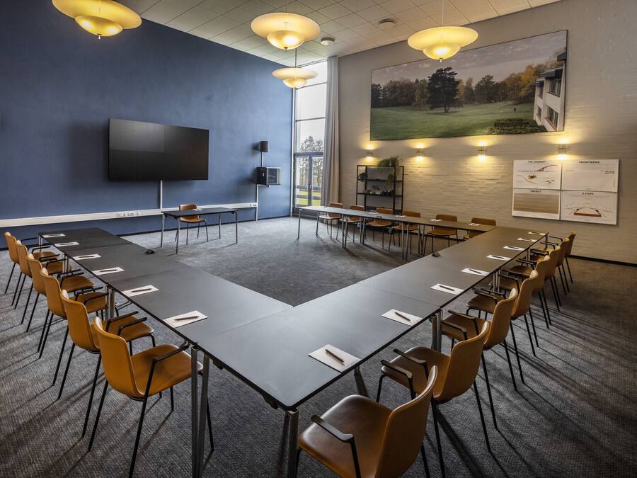Un salón de conferencias con una mesa larga, sillas, un televisor y un ventanal grande.