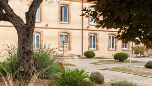 Un bâtiment doté de nombreuses fenêtres, d’une fontaine centrale et d’un jardin bien entretenu, où l’on trouve diverses plantes et arbustes.