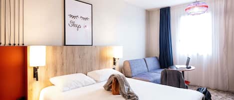 Habitación de hotel con una cama grande, un sofá, una mesita con una computadora portátil y una lámpara colgante decorativa.