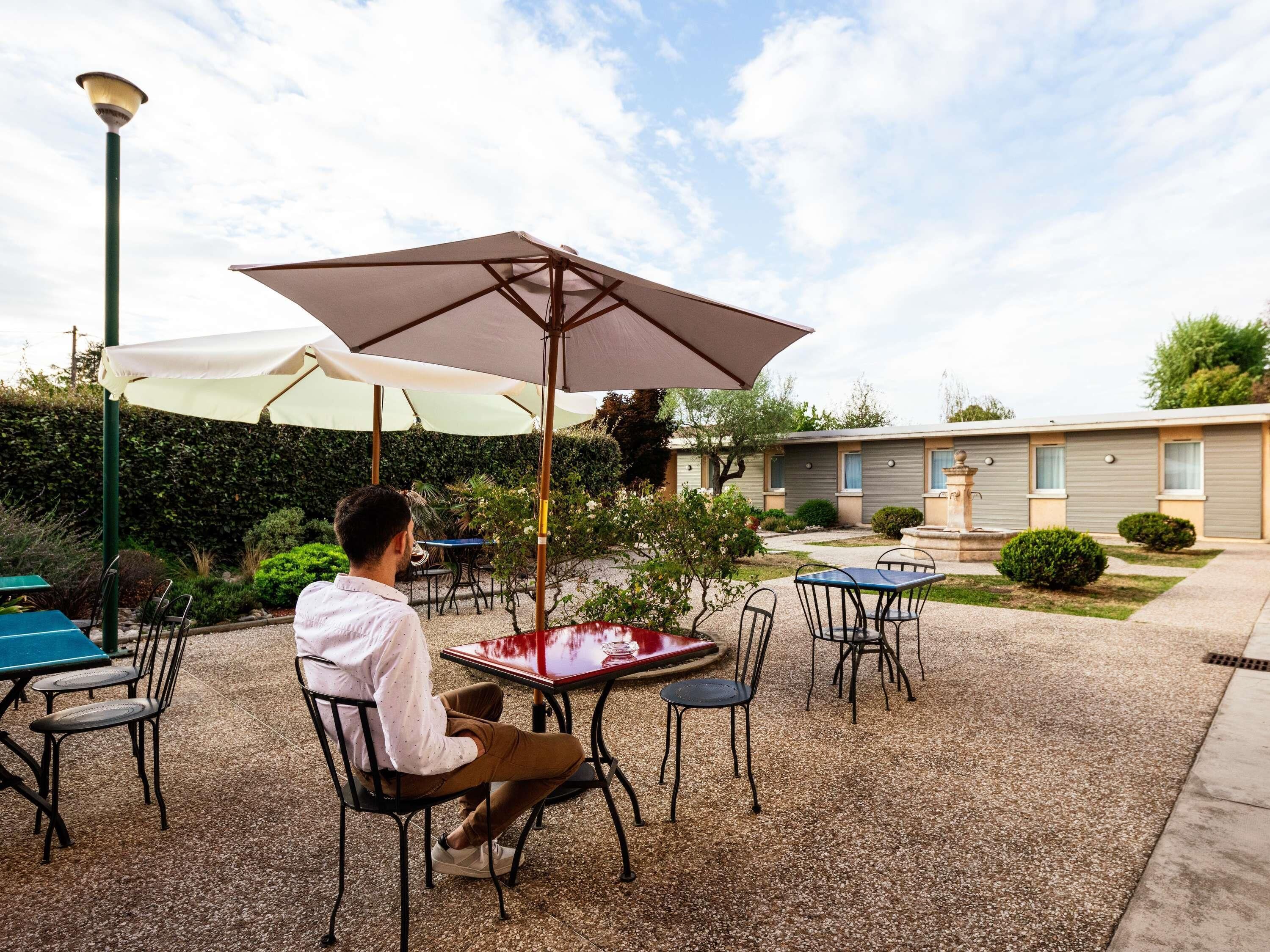 Un espacio patio con mobiliario exterior, mesas y sillas, bajo sombrillas.