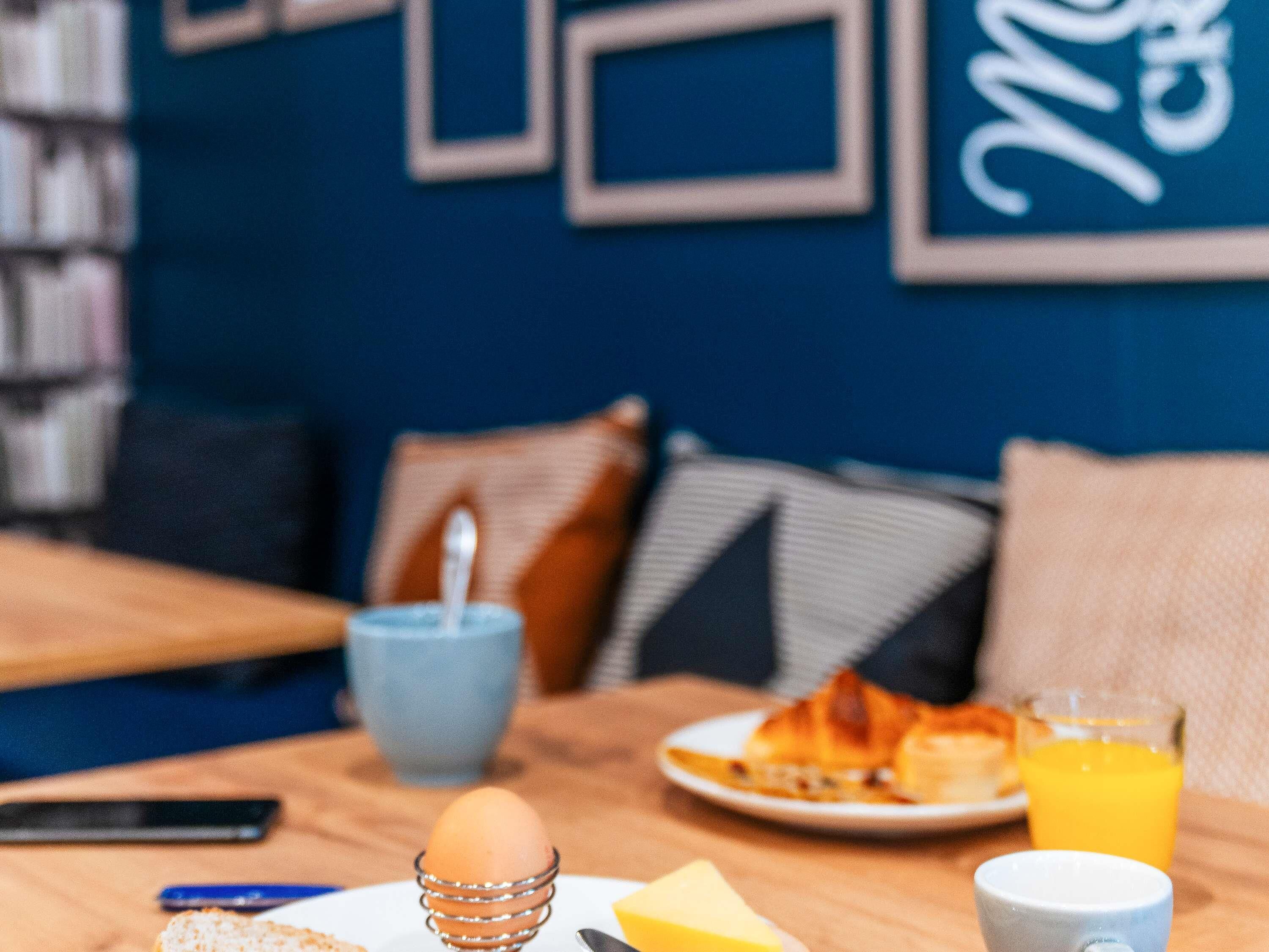 A breakfast setting with a plate of food, a glass of orange juice, and a cup on a wooden table.