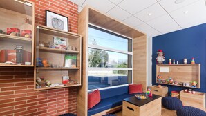 Une pièce chaleureuse avec une grande fenêtre, des étagères en bois, un canapé bleu et une petite table avec des jouets.