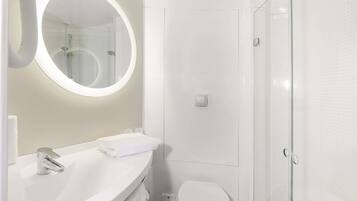 Ein modernes Badezimmer mit rundem Spiegel, Waschbecken in Weiß, Toilette und einer Duschkabine aus Glas.