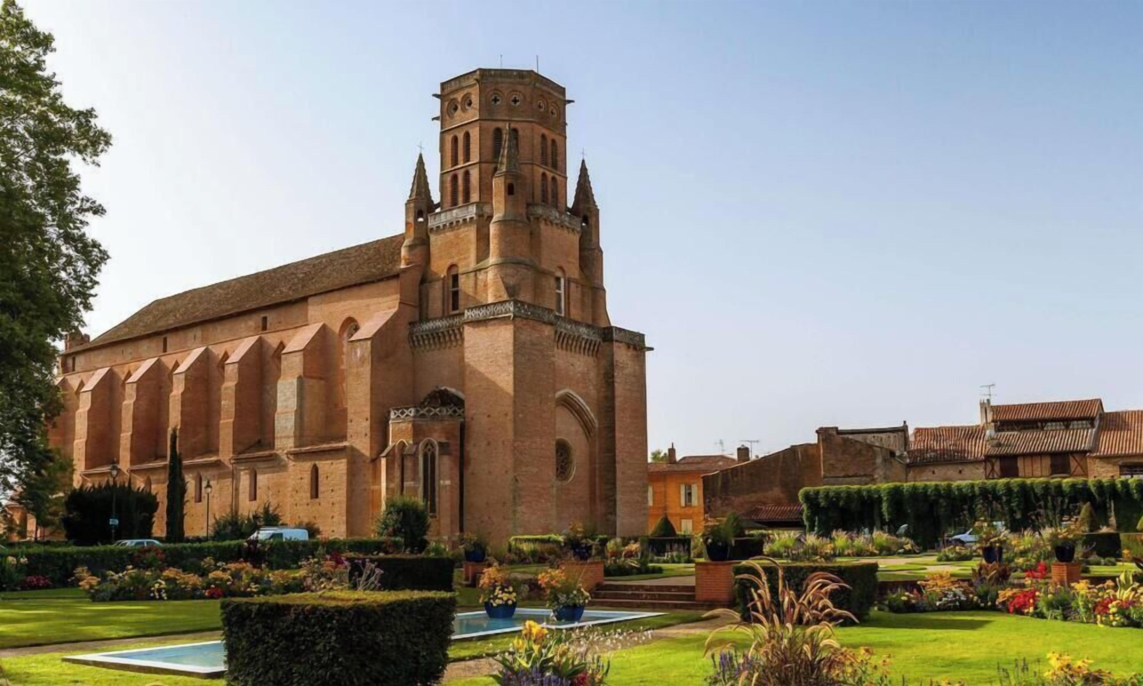 A historic building with a prominent tower, surrounded by well-maintained gardens and a clear sky.