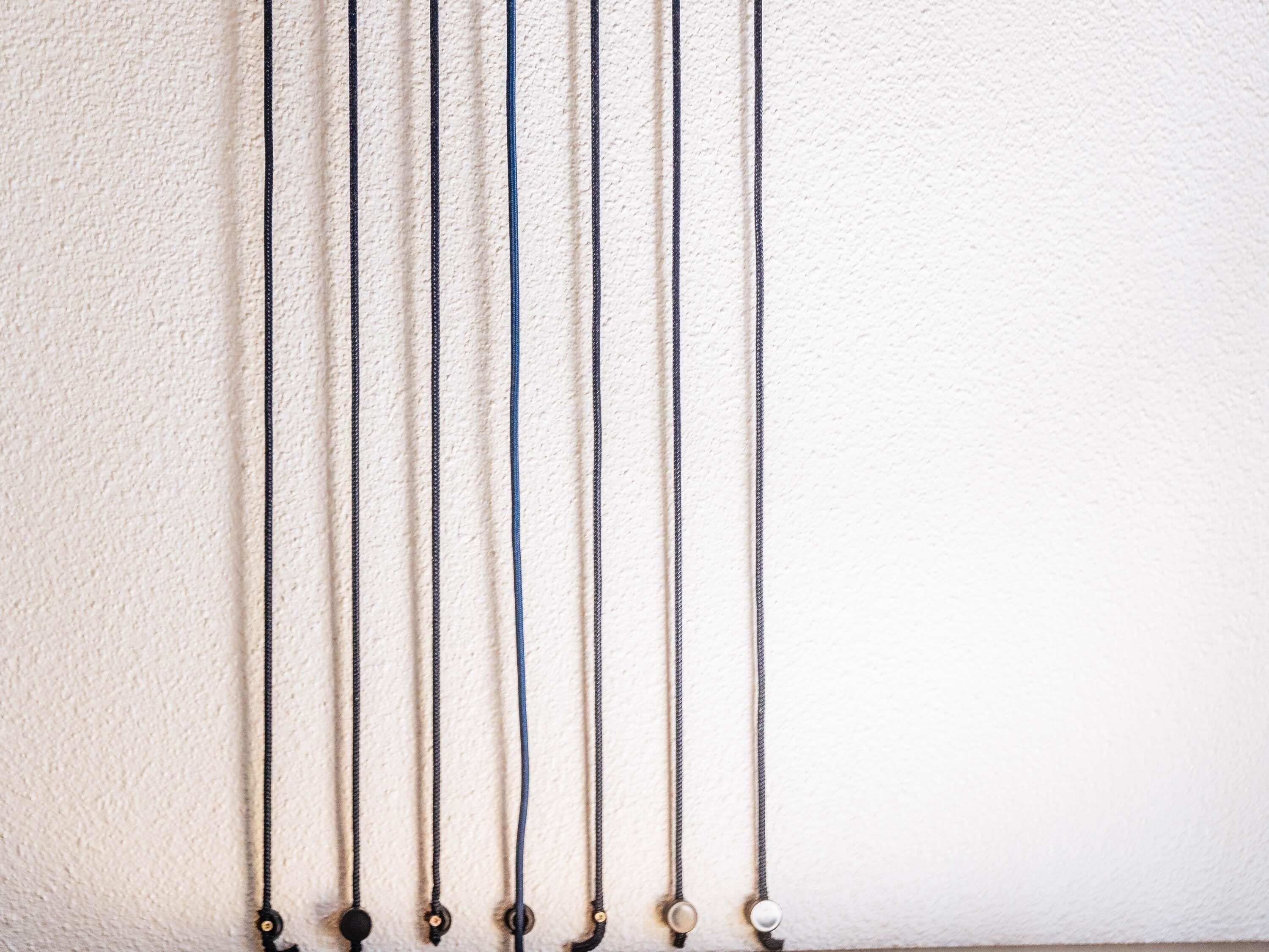 A series of necklaces with varying lengths and designs against a textured wall.