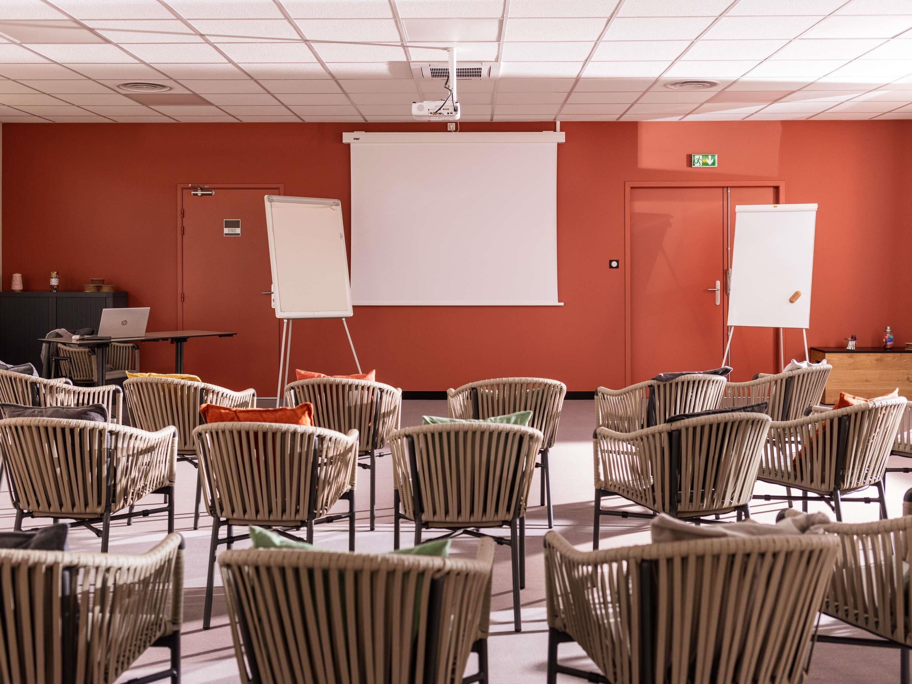 Uma sala de conferências com cadeiras de vime, um quadro branco, um projetor e um laptop sobre uma mesa.