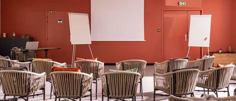 Uma sala de conferências com cadeiras de vime, um quadro branco, um projetor e um laptop sobre uma mesa.