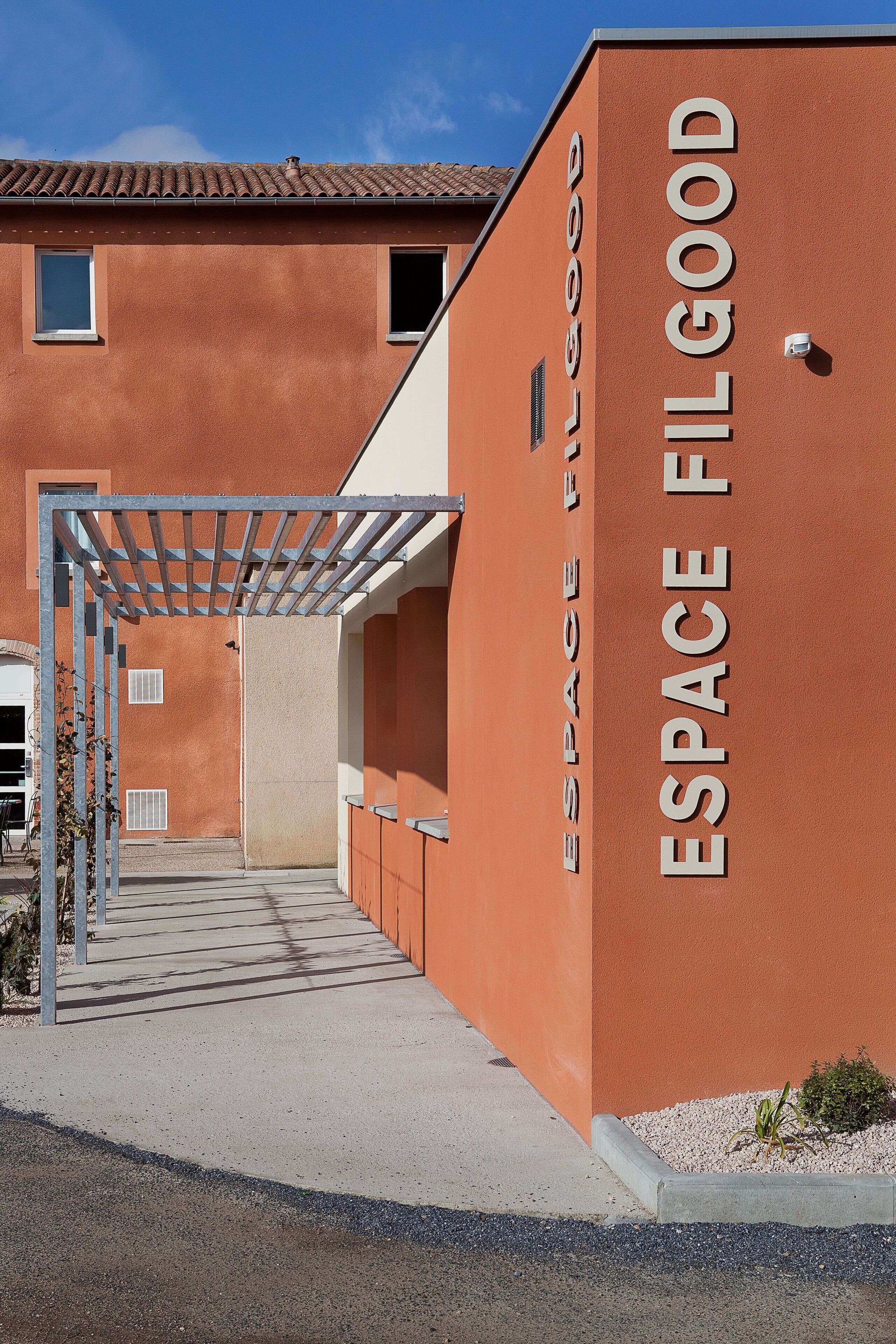 Un edificio de fachada roja con la inscripción "ESPACE FIL GOOD" en la pared.